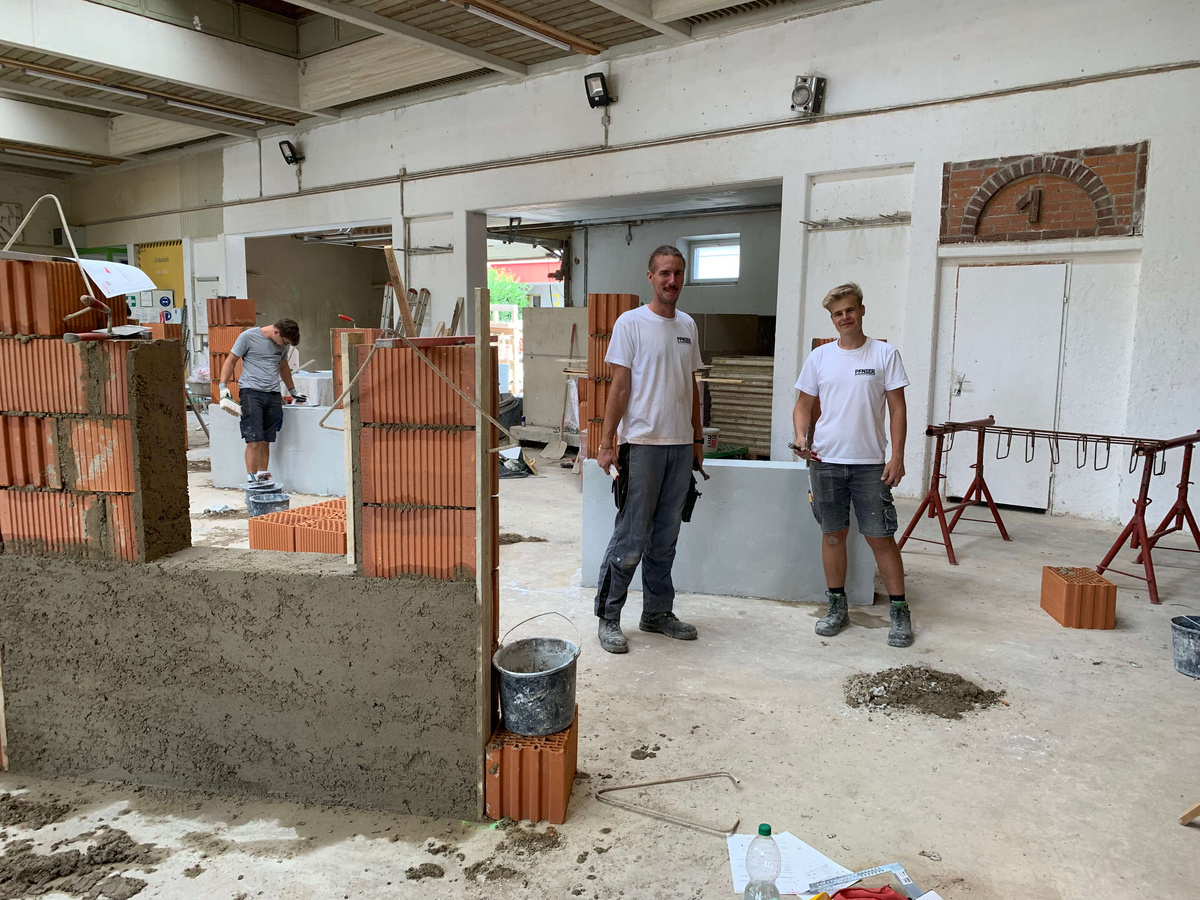 Zwei Lehrlinge in der Bauhalle vor einer gemauerten Übungswand