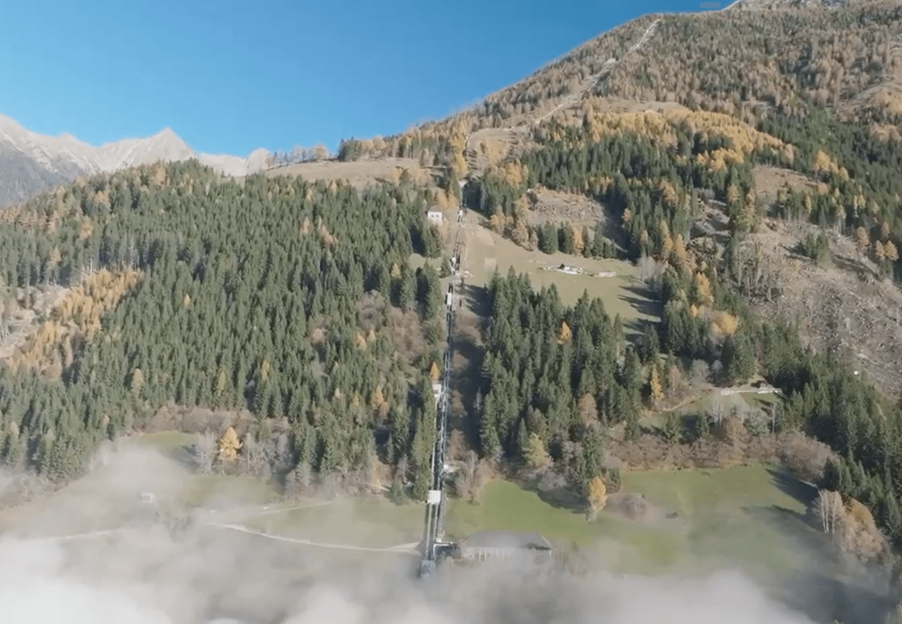 Luftaufnahme eines Bergwaldes mit herbstlich gefärbten Bäumen und ehemaliger Bahntrasse